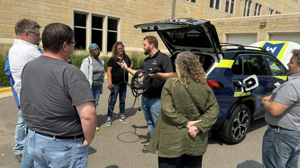 Man explaining electric vehicle car chargers to a group of teachers